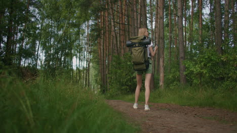 View-from-the-back-mobile-phone-in-the-hands-of-a-female-traveler-with-a-backpack-walking-through-the-forest.-Social-networks-Navigator-and-messenger.-Use-your-mobile-phone-for-a-walk-in-the-woods